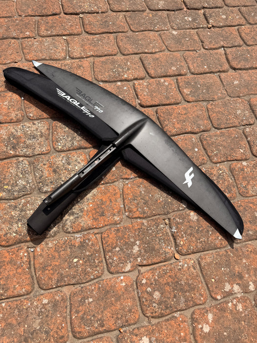 Overview of used F-one Eagle 990 HM Carbon wing foil showing top view with F-one lightning bolt logo and underside view on brick paving