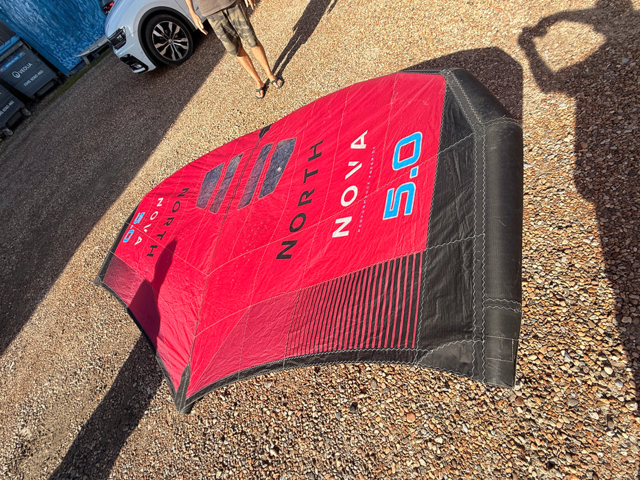 North Nova 5.0 wing foil wing packed into its carry bag, leaning upright against a railing