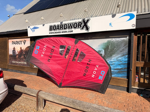North Nova 2023 5.0m wing foil wing laid flat on the ground outside Board-Worx, showing the red canopy underside and NORTH NOVA branding