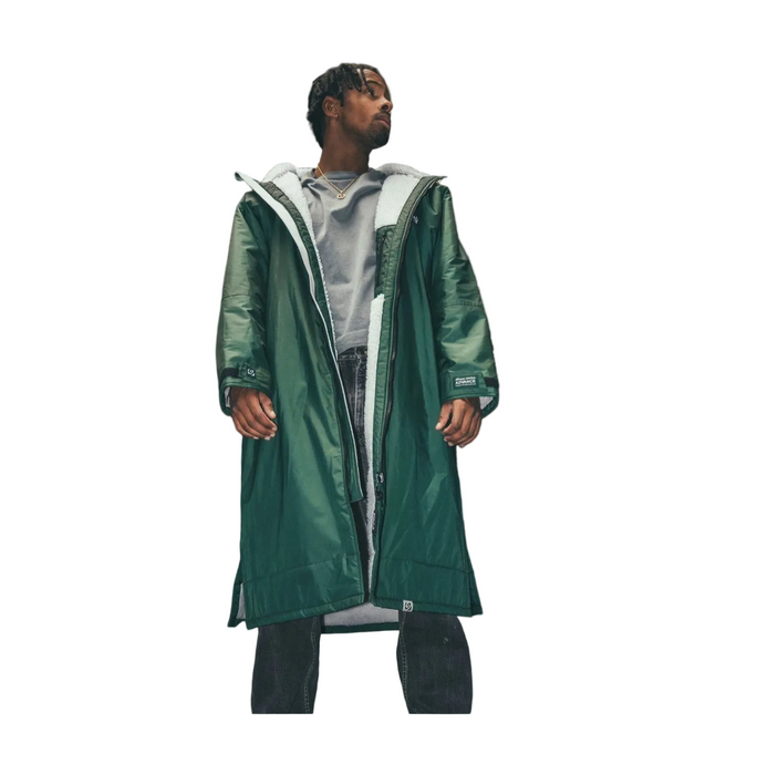 A model wearing a long, dark green dryrobe advanced long sleeve changing robe,hooded raincoat over a light gray hoodie and dark jeans, shown against a plain white background with a black border.