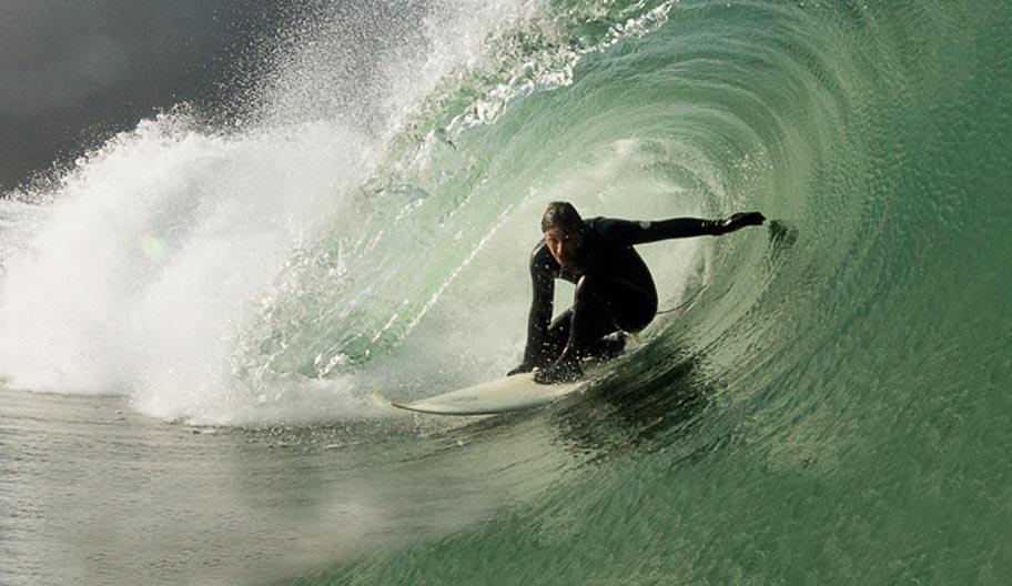 Surfer riding a wave in a wetsuit on a surfboard, product manufacturer and model not visible.
