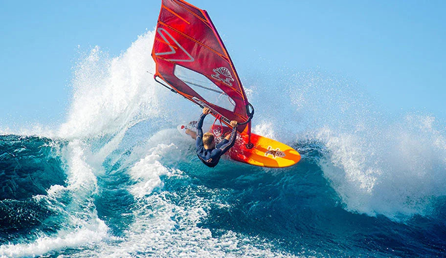 Windsurfer riding a wave on a Starboard Severne windsurf board and red sail