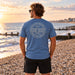 Man wearing the Boardworx Surf Shop indigo blue T-shirt on a Whitstable shingle beach, back logo view