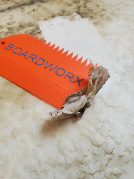 Bright orange BOARDWORX surf wax comb scraper with wax residue on a surfboard