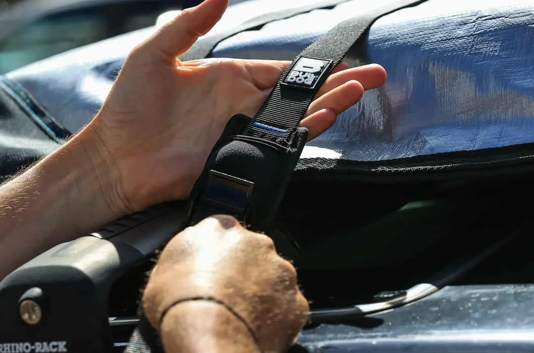 Bulldog black roof rack tie-down strap securing surfboard on car for watersports.