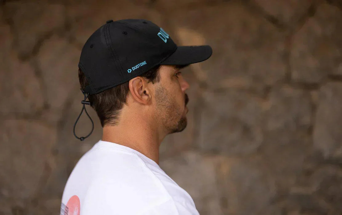 Man wearing black Duotone cap with adjustable strap, side view against stone wall
