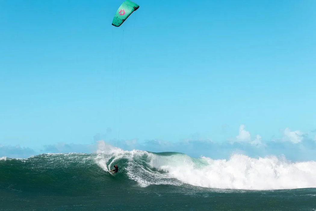 Duotone Neo SLS teal kitesurfing kite in action on ocean waves under clear sky