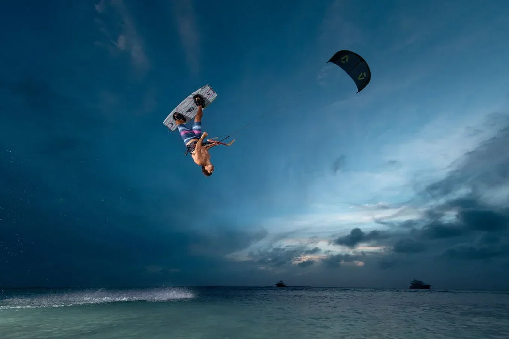 Kitesurfer performing trick with Duotone kite and twintip board over the water at sunset.