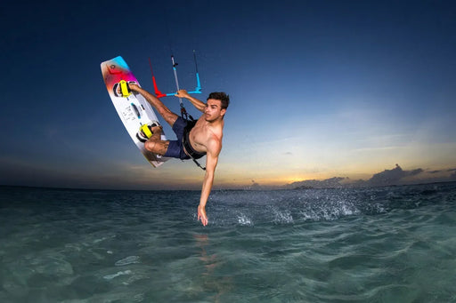 Duotone twin tip kiteboard with yellow foot straps in action, kitesurfer jumping at sunset over clear water.