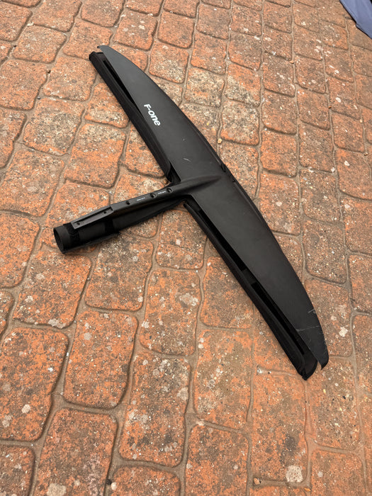 Top view of used F-one Eagle 1290 HM Carbon wing foil front wing on brick paving showing F-one logo and carbon construction