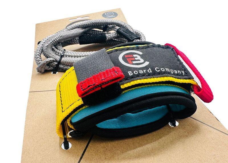 FBC Board Company wrist wing foil leash with yellow, red, and blue padded strap on retail packaging.
