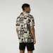 Man wearing sand color graphic surf shirt and black shorts, back view, watersports clothing