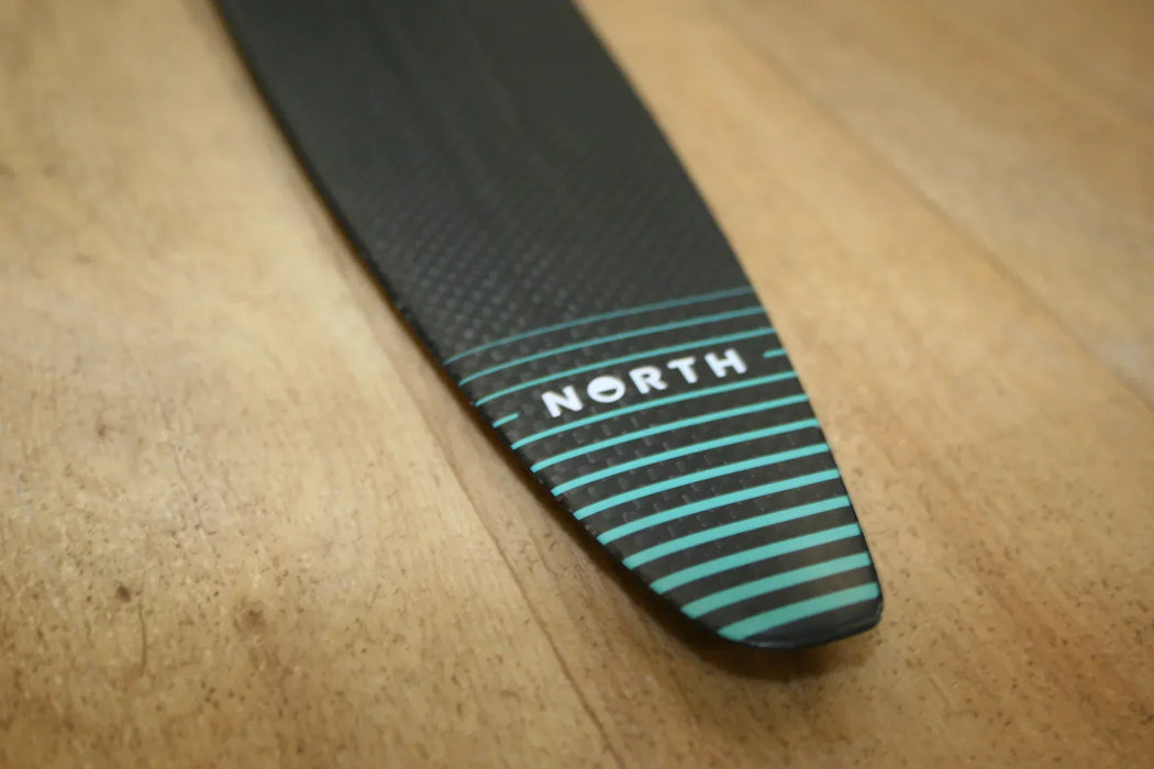 North Sonar S238 stabilizer hydrofoil part, carbon with teal stripes, closeup on wood