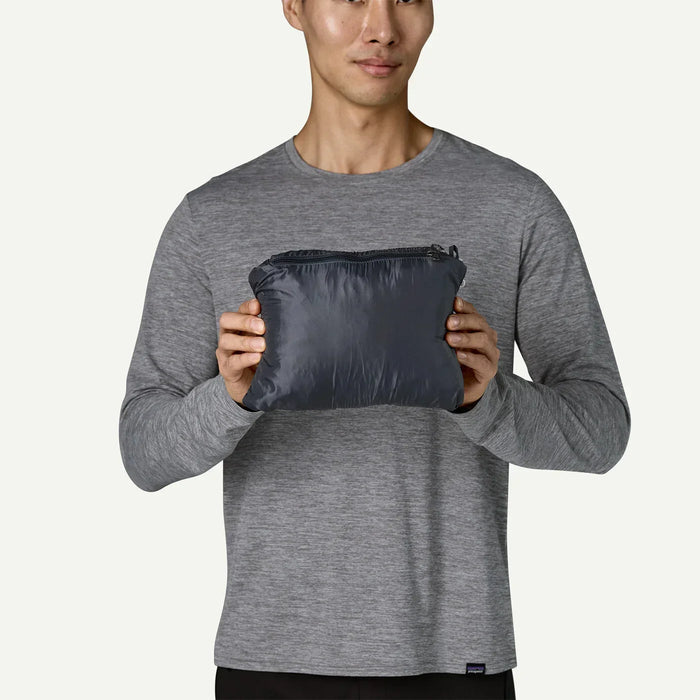 Man holding packed black Patagonia Nano Puff Hoody, compact surf clothing for watersports.