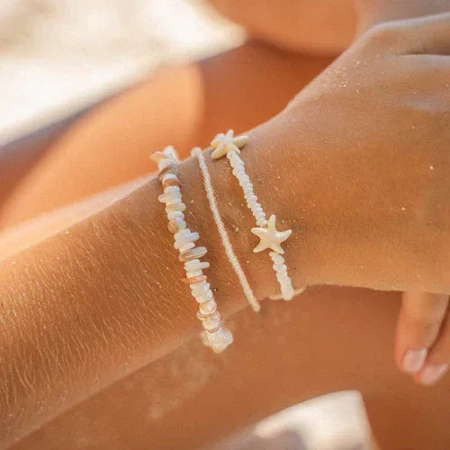 Alona Beach shell bracelet set with starfish charm, natural white beads, on wrist at beach.