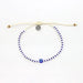 White and blue evil eye anklet with adjustable cord and small round charm, laid flat