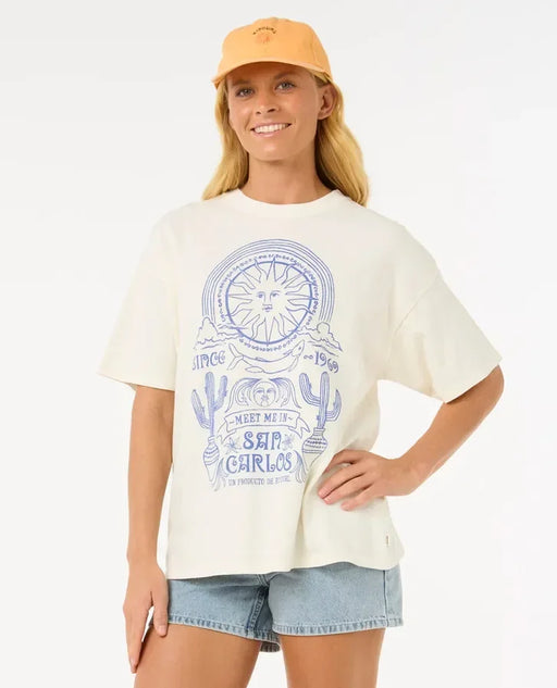 Rip Curl heritage tee in bone with blue sun and cactus print, worn with light denim shorts and yellow cap.