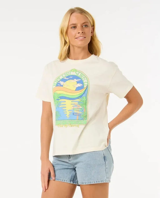 Woman wearing Rip Curl Sun and Sea relaxed fit white surf t-shirt with colorful graphic, paired with denim shorts.