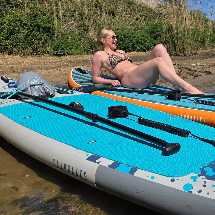 Woman relaxing on a Sandbanks Pro X Turquoise inflatable paddle board by the water