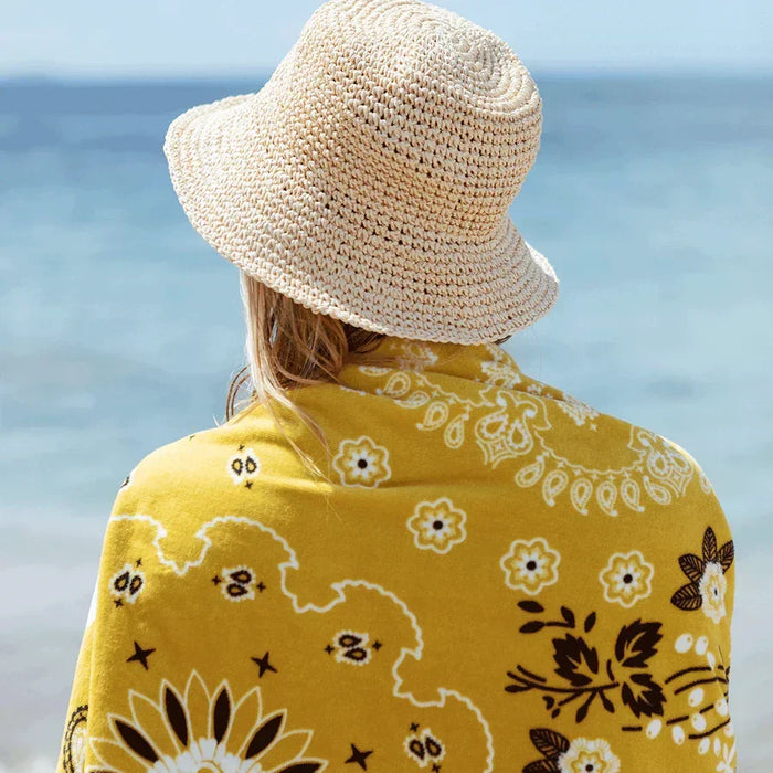 Slowtide Axel beach towel yellow floral pattern by the sea, person in straw hat