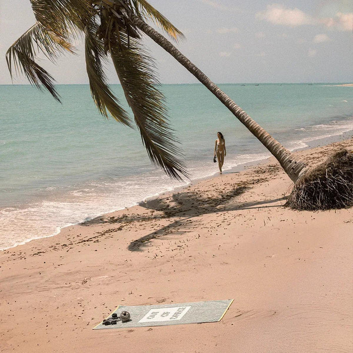 Slowtide Out of Office premium woven towel in green on sandy beach with palm tree