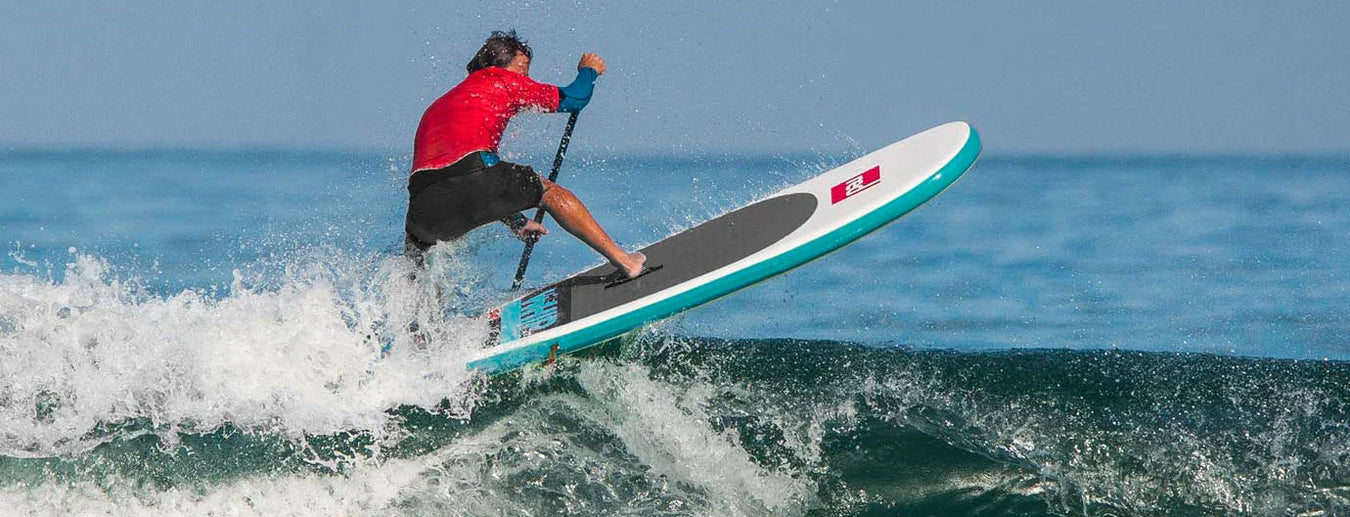 Starboard SUP paddle board rider surfing on ocean wave, Starboard logo visible on deck