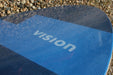 Vision blue skimboard with textured surface on pebbles, brand name visible.