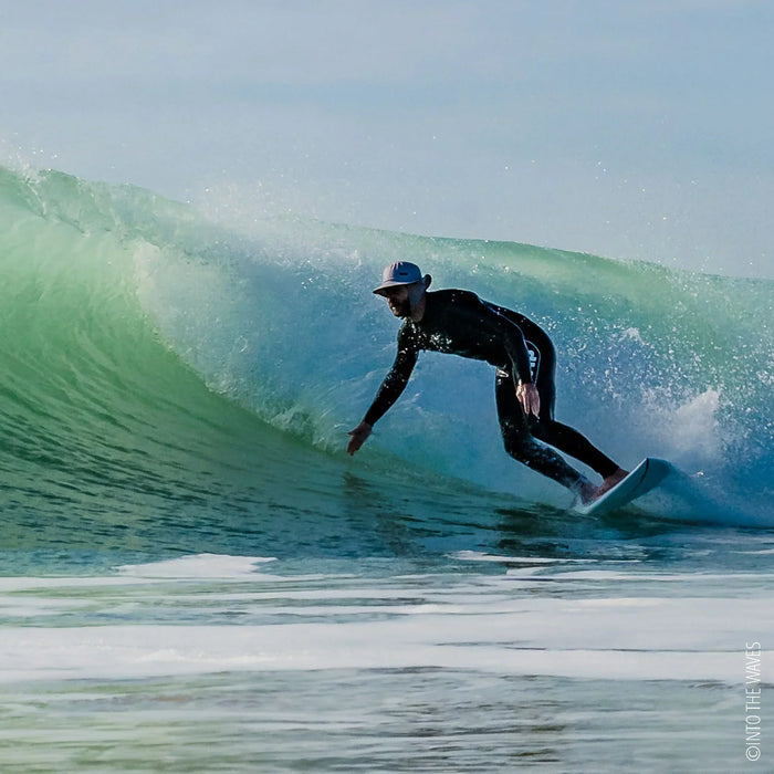 Surfer wearing black wetsuit and white shell hat riding wave on surfboard