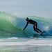 Surfer wearing black wetsuit and white shell hat riding wave on surfboard